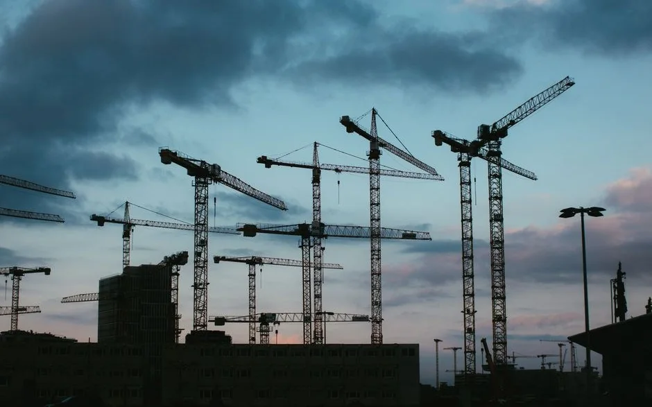Alacakaranlıkta bulutlu gökyüzüne karşı silueti çıkan inşaat vincleri