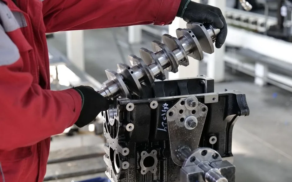 Kırmızı iş tulumlu bir teknisyenin motor bloğuna krank mili yerleştirmesi