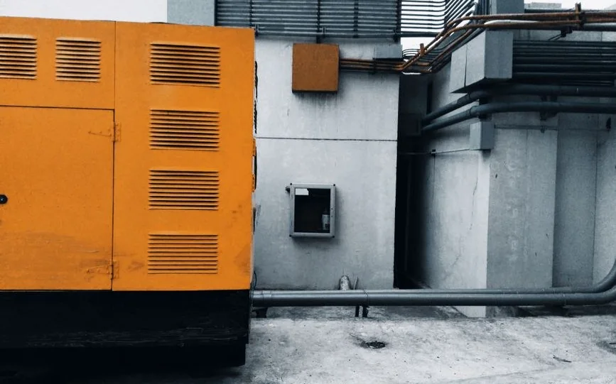Beton bir tesis duvarının yanına kurulmuş turuncu kabinli sessiz tip jeneratör